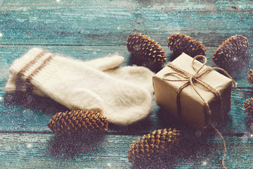 gift box,mittens and pine cones on a blue wooden boards. toned. painted snow.