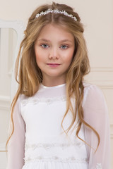 beautiful girl little princess long hair, curly and amazing blue eyes in communion dress and tiara on his head, sitting in elegant palatial room with a dressing table with mirror in the background © marcink3333