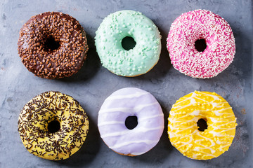 Variety of colorful glazed donuts over gray metal texture background. Top view