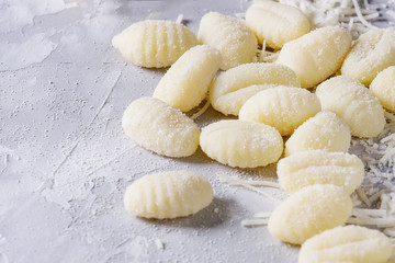 Raw uncooked potato gnocchi with flour and grated parmesan cheese over gray concrete background. Close up. Home cooking.