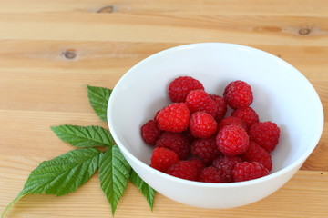 fresh red raspberry fruits in a small white bowl