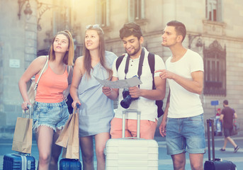 four cheerful travelers holding map in hands and looking for the