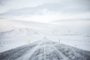 Straight road in snow covered landscape and stormy weather, Route 1, western Iceland