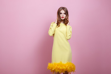 Cheerful beautiful young stylish woman in yellow dress posing on pink background and looking at camera. Smilling lady. Studio photo.
