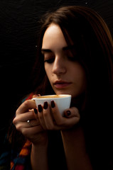 young pretty girl with wrap on her shoulders holding a cup of coffee thoughtfully looking into the cup, cute portrait
