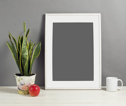 White frame mockup with plant pot, mug and apple on wooden shelf.