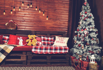 Beautiful Christmas interior design. Room decorated with wooden sofa with warm blanket, lights, teddy bear and wooden horse, toned image. Concept of Merry Christmas, winter and New year