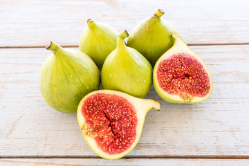 Whole figs and one fig sliced in half on top of a  garden table. Focus is on the sliced fig.