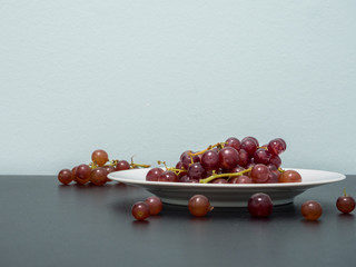 Purple grapes on white plate on the black table