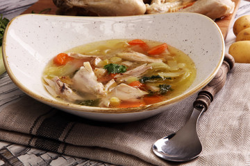 Bone broth made from chicken with carrots, onions various fresh vegetables in a pot - colorful fresh clear spring soup. Rural kitchen scenery bouillon or stock