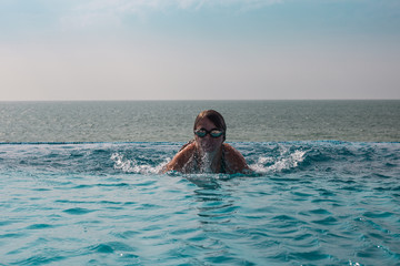 Girl in glasses in a swimming pool with ocean view