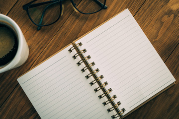 White Cup of coffee, eyeglasses, notepad, on brown wooden table background in coffee shop