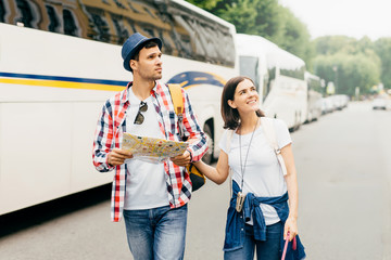 Obraz premium Young hiking couple going through big city, looking attentively aside, using city guide for exploration new places on map. Family couple having journey together during their summer vacations