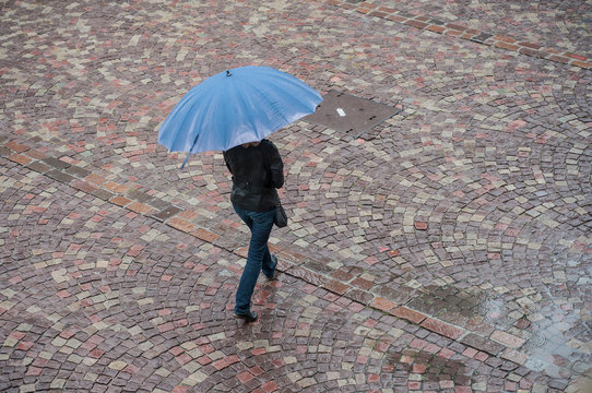 femme traversant une place pavés avec un parapluie