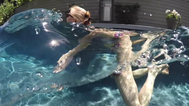 Camera half above and half below water, a beautiful, slim, caucasian woman wearing string bikini swims from right to left. Camera follows her.