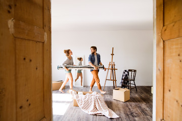 Young couple moving in new house, carrying a carpet.