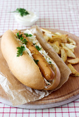 Hot dog with sausage and salad, served with french fries, mustard and mayonnaise sauce. Rustic style, selective focus.