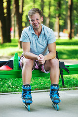 Portrait of happy handsome male roller sitting on bench in the park.