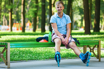 Portrait of happy handsome male roller sitting on bench in the park.