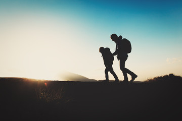 Fototapeta premium Silhouettes of father and son hiking in sunset mountains
