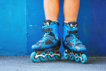 Closeup photo of legs in blue inline skates standing against blue wall.