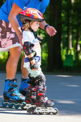 Cute baby boy with inline skating instructor in the park learining to skate.