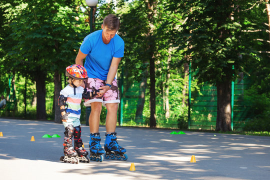 Cute baby boy with inline skating instructor in the park learining to skate.