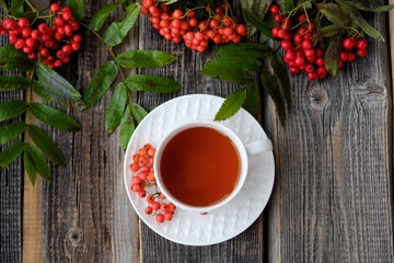 Delicious cup of tea and Rowan berries on a wooden table