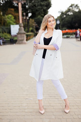 American Woman with high heels, arm carrying bag, a lady with blonde hair standing on street.