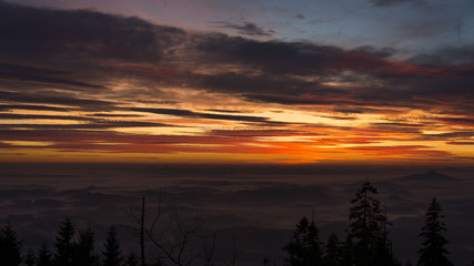 Fototapeta na wymiar Strong orange sunset over landscapes hidden under fog.
