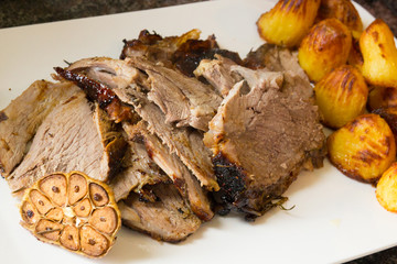 lamb roast carved on plate with roast potatoes and garlic