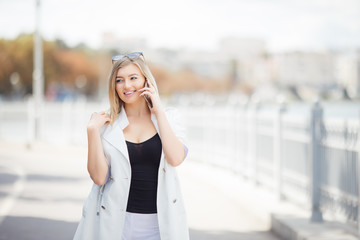 Fototapeta premium beautiful young woman talking on the phone in the city walking on embankment