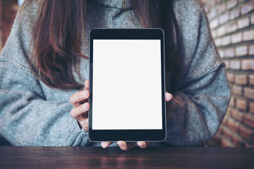 Mockup image of a woman holding and showing black tablet pc with blank white screen in modern cafe...