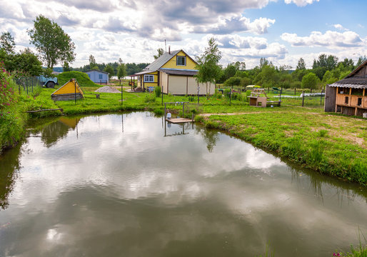 Wooden village house with outbuildings and small pond in summertime