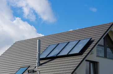 Photovoltaics on new build house roof with blue sky and aluminium chimney
