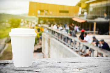 paper coffee cup with tasty hot coffee on wooden table outdoors with blur focus outdoor public area on road trip in thailand