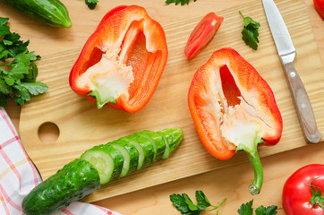 Two halves of red pepper and chopped cucumber on the kitchen board