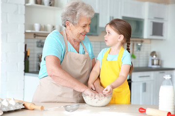 Cute little girl and her grandmother cooking on kitchen