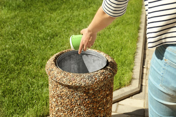 Young woman throwing paper cup in litter bin outdoors