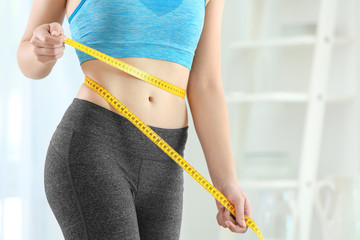 Young woman with measuring tape at home. Diet concept