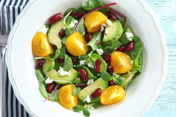Superfood salad with yellow tomato, beans and zucchini in white ceramic plate, top view