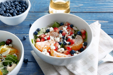 Superfood salad with tangerine, blueberries and pomegranate seeds in white bowl on wooden background