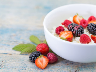 Organic cottage cheese with blackberry, strawberry and raspberry in a white ceramic bowl on the kitchen table. Dairy products for the breakfast. Healthy food concept