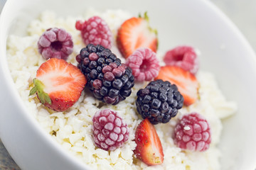 Organic cottage cheese with blackberry, strawberry and raspberry in a white ceramic bowl on the kitchen table. Dairy products for the breakfast. Healthy food concept.