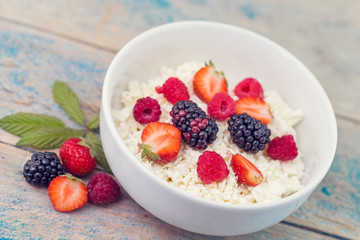 Organic cottage cheese with blackberry, strawberry and raspberry in a white ceramic bowl on the kitchen table. Dairy products for the breakfast. Healthy food concept