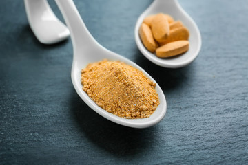 Camu powder and pills in white ceramic spoons on dark background