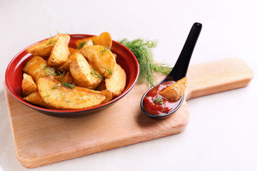 Bowl with delicious baked potato wedges on wooden board