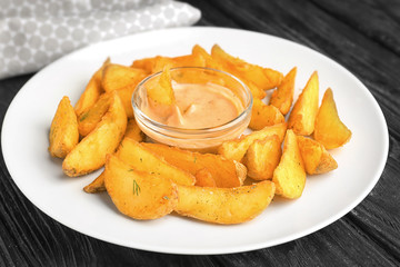 Plate with delicious baked potato wedges and sauce on table