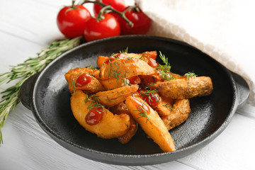 Frying pan with delicious baked potato wedges on table