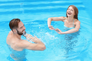 Happy young couple playing in swimming pool